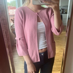 Trekvartsärmad kofta - Rosa Trekvartsärmad kofta med rosetter på ärmarna. Knäppa med en knapp upptill. Perfekt nu till hösten! Skicket är mycket bra. 