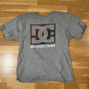 DC Shoes T-shirt Grey - Säljer en grå t-shirt från DC Shoes med stort tryck på framsidan. T-shirten har en klassisk passform och är tillverkad i mjukt material. Perfekt för en avslappnad stil.