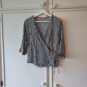 Svartvit randig omlottblus - Snygg svartvit randig omlottblus med trekvartsärm och knytband i midjan. Perfekt för en stilren look.