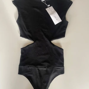 Svart body från Amisu - Snygg svart body från Amisu med stilren design. Den har en unik skärning i midjan som ger en modern look. Aldrig använd då den inte kommit till användning!