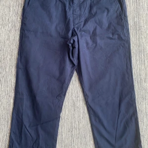 Mörkblå chinos från Gant w40/L32 - Snygga mörkblå chinos från Gant med en klassisk design. Byxorna har en knapp och dragkedja framtill samt två bakfickor med knappar. Perfekta för en stilren look. Marinblåa chinos i strl W40/L32 från Gant, modell regulator.  Endast använda vid ett par tillfälle och är i fint begagnat skick.  Mått Midjan: ca 53 cm Från grenen och ner: ca 68 cm  100% bomull   Kommer från ett djur och rökfritt hem.