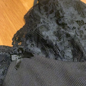 Spets linne - Ribbat linne med spets och en liten rosett. Det är svart och dras ihop vid sidorna. I storlek S åt det större hållet. 