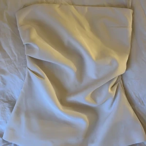 Vit tubtopp från Zara - Säljer en stilren vit tubtopp från Zara. Toppen är axelbandslös och har en elegant passform som passar perfekt för olika tillfällen. Tillverkad i ett mjukt material för en bekväm känsla.