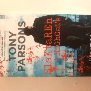 Slaktaren i Highgate - Boken 'Slaktaren i Highgate' av Tony Parsons är en spännande thriller. Omslaget har en dramatisk design med blodstänk och en mörkklädd figur mot en bakgrund av en stadsmiljö. Perfekt för dig som gillar kriminalromaner med en intensiv handling.