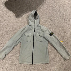 Grå/grön stone Island jacka - Säljer min jacka från Stone Island. Köpt på NK i Göteborg. Otroligt bra skick, ända e svarta på vänster underarm som kan ses på bild 4. Authentication kan ni se på bild 5 och scanna själva om ni så vill det. Jackan är junior storlek och passar dig som är mellan 165-175 beroende på kroppsbyggnad.