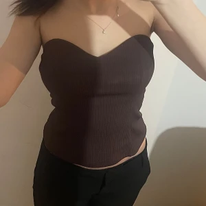 Brun ribbad tubtopp från river island - Gåva på köpet! Säljer en stilren brun ribbad tubtopp. Toppen är axelbandslös och har en tight passform som framhäver figuren. Perfekt för utekväll/middag 🫶🏻