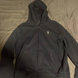 Svart zip hoodie från Polo Ralph Lauren - Säljer en stilren svart hoodie från Polo Ralph Lauren med dragkedja och klassisk logga på bröstet. Bara använd ett fåtal gånger, pris kan sänkas vid snabb affär.