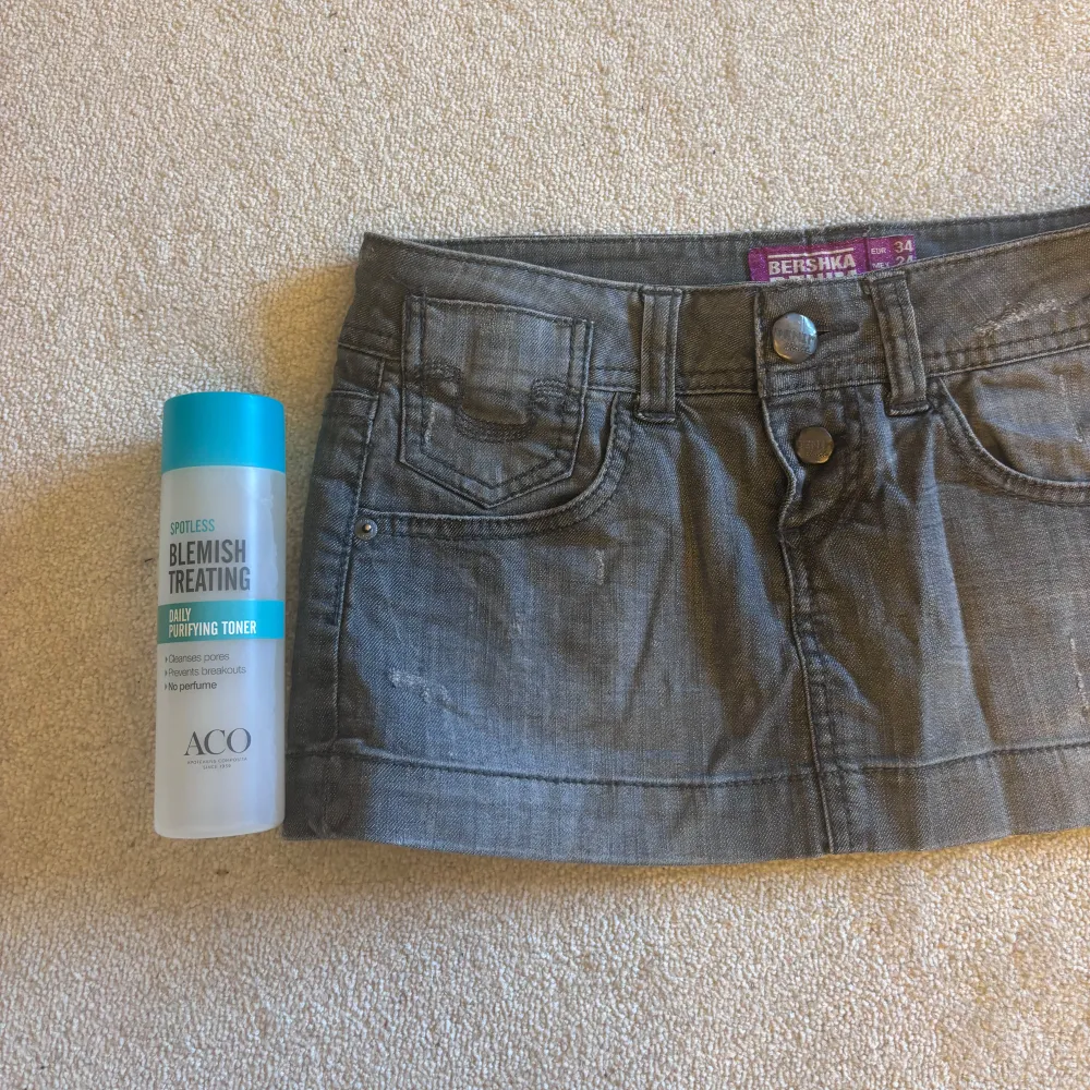 Säljer en snygg grå jeanskjol från Bershka. Kjolen har en klassisk femficksdesign med två knappar framtill. Perfekt för en avslappnad stil. Väldigt kort, ni ser jämförelse med toner flaska på sista bilden. Även lågmidjad.Skit snygg till sommar, höst. Säljer pågrund av flytt och för mycket kläder☺️☺️. Hameet.