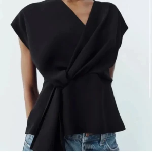 Svart omlottopp - Snygg svart omlottopp med knytning i midjan. Toppen har en elegant v-ringning och korta ärmar, perfekt för en stilren look. Passar bra till både jeans och kjol.