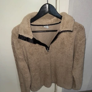 Beige och svart fleecejacka med dragkedja - Två mysiga fleecejackor i beige och svart med dragkedja. Perfekta för kyliga dagar. Den beige har en mjuk och fluffig textur medan den svarta är stilren och enkel. Båda har en hög krage för extra värme. Den svarta är Xs och den beigea är M