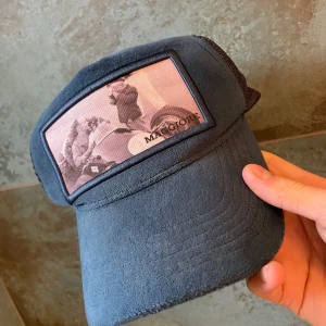 Blå keps från Maggiore - Snygg blå keps från Maggiore med ett unikt tryck på framsidan. Kepsen har en justerbar orange rem baktill för perfekt passform. Perfekt för en avslappnad stil.