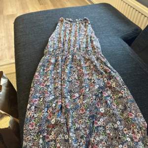 Säljer en söt blommig klänning med hög hals och elastisk midja. Klänningen har ett färgglatt blommönster i rosa, blått och grönt på en mörk bas. Perfekt för sommarens alla tillfällen! 🌸