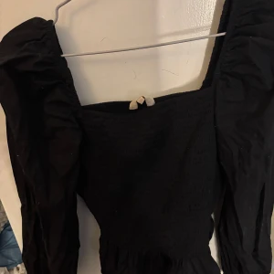 Svart topp från Pernilla Wahlgren - Snygg svart topp från Pernilla Wahlgren med smockdetaljer och långa puffärmar. 