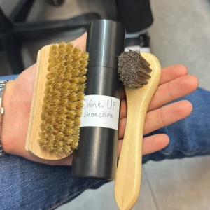 Skovårdskit med borstar och spray - Praktiskt skovårdskit från Shine. UF som innehåller en svart sprayflaska för skovård samt två olika borstar. Den ena borsten har ett större handtag och täta borst, medan den andra är mindre med ett rundat huvud. Perfekt för att hålla dina skor i toppskick.
