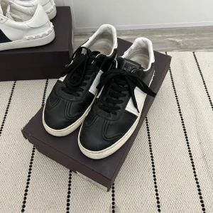 Svarta och vita sneakers från Valentino - Snygga svarta och vita sneakers från Valentino med klassisk design. Skorna har snörning och en vit sula som ger en stilren look. Perfekta för en trendig vardagsstil.