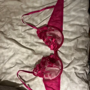 Rosa spets-bh från Ell M - Säljer en snygg rosa bralette från Ella M med spetsdetaljer och justerbara axelband. Den har en transparent design med blommönster.