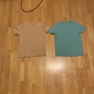 Två t-shirts från H&M i beige och turkos - Säljer två t-shirts från H&M i storlek 146/152. Den ena är beige och den andra är turkos. Perfekta för en avslappnad stil. Båda är kortärmade och gjorda i mjukt material.