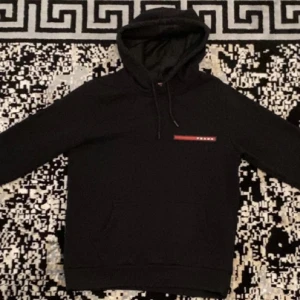 Svart hoodie från Prada - Säljer en stilren svart hoodie från Prada med en liten logga på bröstet. Den har en klassisk design med huva och dragsko samt en praktisk magficka. Perfekt för en avslappnad look.Endast seriösa köpare snälla om du inte ska köpa är det ingen mening du dmar mig!