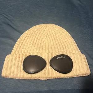 Beige ribbad mössa från C.P. Company - Snygg vit ribbad mössa från C.P. Äkta köpt på NK Göteborg 9av10 skick har en liten repa på insidan men inget man ser. Nypris 1600kr 
