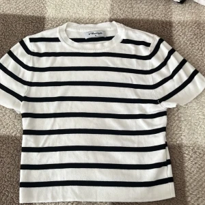 Randig t-shirt från Maariyah - Säljer en stilren vit och svart randig t-shirt från Maariyah. Den har en klassisk rund halsringning och korta ärmar. Perfekt för en avslappnad look.