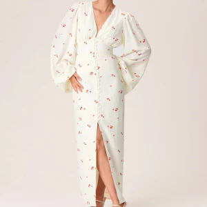 Vit blommig långklänning - Elegant vit långklänning med små röda blommor. Klänningen har långa ärmar och en slits framtill, Perfekt till sommaren. Från adoore, klänningen är i fint skick då den endast är använd tre gånger❣️tyget på en av knapparna har lossnat (inget som syns), se bild ovan. slutsåld på hemsidan.