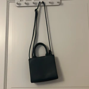 Svart axelväska - Snygg och stilren svart axelväska med justerbar rem och handtag. Perfekt för att bära dina nödvändigheter med stil. Väskan har en enkel och elegant design som passar till många olika tillfällen.