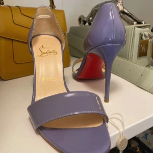 Lila klackskor från Christian Louboutin - Snygga lila klackskor från Christian Louboutin med den ikoniska röda sulan. Skav på ena hälen som syns på när håll, därav priset. Äkthets verifierat av Vestiaire Collective