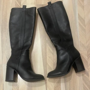 Svarta stövlar med klack - Snygga svarta stövlar i skinn med hög klack. Perfekta för en stilren look. De har en elegant design med rundad tå och är lätta att matcha med olika outfits.