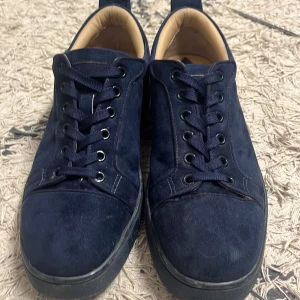 Mörkblå sneakers med röd sula - Snygga mörkblå sneakers i mocka med svart snörning och en iögonfallande röd sula. Skorna har en diskret logga på hälen och en bekväm passform. Perfekta för en stilren look.