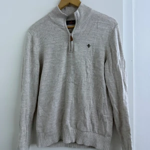 Beige tröja från Morris - Säljer en stilren beige tröja från Morris med dragkedja vid halsen och ett diskret emblem på bröstet. Tröjan har långa ärmar och ribbade muddar vid ärmslut och nederkant. Perfekt för en avslappnad men snygg look.