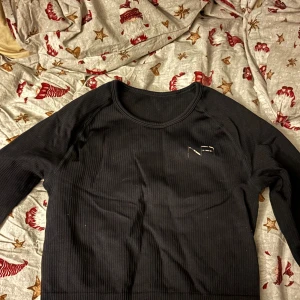 Svart ribbad tränings tröja  - Snygg svart ribbad tröja från Ullared med rund halsringning. Perfekt för en stilren look. Tröjan har långa ärmar och en diskret logga på bröstet. Storleken är Xs