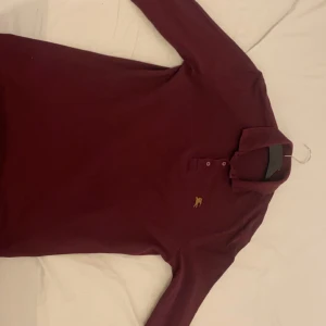 Vinröd pikétröja från Burberry - Snygg vinröd pikétröja från Burberry i 100% bomull. Tröjan har långa ärmar och en klassisk krage med knappar. Perfekt för en stilren look.