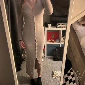 Beige ribbad klänning från H&M - Säljer en stilren beige ribbad klänning från H&M. Klänningen har en v-ringad design med knappar längs hela framsidan och långa ärmar. Perfekt för en elegant och bekväm look. Skriv för mer information💕