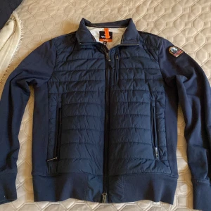 Mörkblå jacka från Parajumpers - Säljer en snygg mörkblå jacka från Parajumpers i mycket bra skick. Köpt för 1 år sedan och är använd 1-2 gånger. Jackan har en quiltad design med dragkedja och långa ärmar. En stilren look och praktiska fickor med dragkedjor. (säljer för att jag köpte fel storlek) köpt för 5000 men säljer för mycket mindre 