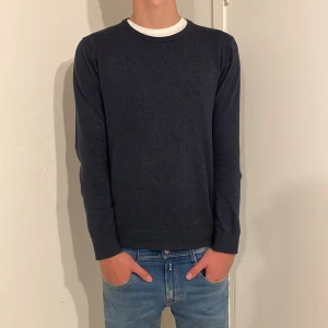 Mörkblå tröja från Lindbergh - Snygg mörkblå tröja från Lindbergh med rund halsringning. Perfekt för en stilren look. Tröjan har långa ärmar och är tillverkad i ett mjukt merinoull material. Passar både till vardag och fest, perfekt under vinterjackan. Orginalpris 599, vårt pris 349.