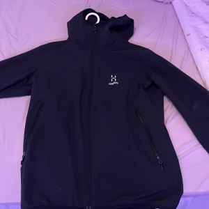 Svart jacka från Haglöfs - Säljer en svart jacka från Haglöfs i storlek XL. Jackan har en huva och dragkedja framtill samt två sidofickor med dragkedjor. Perfekt för utomhusaktiviteter.