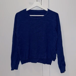 Blå stickad tröja - Säljer en snygg blå stickad tröja med rund halsringning. Tröjan har långa ärmar och ribbade muddar vid ärmslut och nederkant. Super skönt material. Lite längre baktill än fram, med två slitsar på sidorna utav tröjan också.