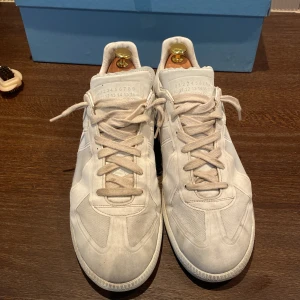 Maison margiela gats - Säljer ett par stilrena vita sneakers från Maison Margiela i bra skick. De är tillverkade i Italien och har en klassisk design med snörning. Perfekta för både vardag och festliga tillfällen. Skorna är jävligt sköna, finns inte skönare på marknaden. Men dem går också bra till alla olika outfits. Skorna är såklart äkta. Ni kan legitchecka hur mycket ni vill men inget OG tillkommer. Priset är samt ej hugget i sten!. Hör av er för minsta frågor eller funderingar.