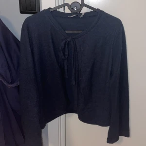 Mörkblå tröja med knytband - Säljer en mörkblå tröja med knytband vid halsen. Tröjan har långa ärmar och är tillverkad i ett mjukt material som ger en bekväm passform. Perfekt för kyligare dagar.