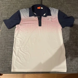 Pikétröja från Puma - Säljer en snygg pikétröja från Puma i storlek L. Tröjan har en cool gradientdesign i vitt och rött framtill och är mörkblå på baksidan. Den har korta ärmar och en klassisk krage med knappar. Perfekt för både träning och vardag! Pris går alltid att förhandlas! 