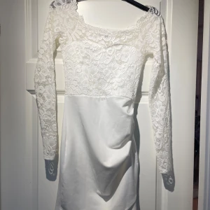 Vit spetsklänning från NLY One - Elegant vit klänning från NLY One med vacker spetsdetalj på överdelen och långa ärmar. Perfekt för speciella tillfällen med sin stilrena design och mjuka material.