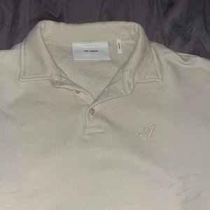 Beige tröja från Axel Arigato - Säljer en stilren tröja från Axel Arigato. Tröjan har en klassisk krage och knappslå framtill. Den är avslappnad men ändå snygg. Storleken är L