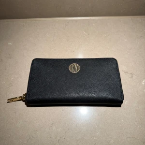 Svart plånbok med dragkedja - Plånbok från DKNY små slitningar vid logotyp. Plats för både kort och kontanter finns. 20 x 10,5 x 2 cm.