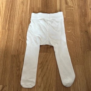 Vita strumpbyxor från Newbie - Säljer ett par vita strumpbyxor från Newbie i storlek 62/68. De är mjuka och bekväma med en söt spetsdetalj på baksidan. Perfekta för att hålla de små varma och stiliga.