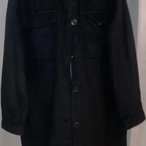 Svart långärmad jacka - Snygg svart jacka med knappar framtill och två bröstfickor. Perfekt för en stilren look. Långärmad design som passar bra till kyligare dagar.