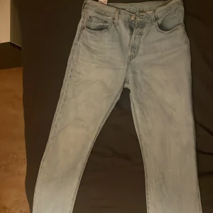 Ljusblå Levis jeans - Säljer ett par klassiska ljusblå Levis jeans i modell 501. De har en rak passform och är högmidjade med fem fickor och knappgylf. Perfekta för en avslappnad stil. De är använda endast ett par fåtal gånger och är i jättebra skick!