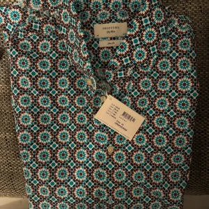 Helt ny Mönstrad skjorta från Profuomo - Snygg skjorta från Profuomo med ett färgglatt geometriskt mönster i brunt, turkos och vitt. Skjortan har långa ärmar och knappar framtill. Perfekt för att liva upp garderoben!