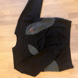 REWORK- GANT Svart tröja från Gant med grå detaljer - Snygg svart tröja från Gant med grå ribbade detaljer på bröstet och ärmarna. Tröjan har en rund halsringning och ett broderat märke på bröstet. Perfekt för en stilren look.