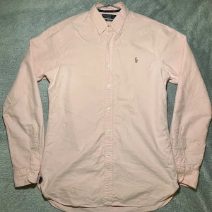 Rosa skjorta från Polo Ralph Lauren - Snygg rosa skjorta från Polo Ralph Lauren i slim fit. Skjortan har långa ärmar och klassisk krage med knappar. Perfekt för en stilren look. Storlek M 