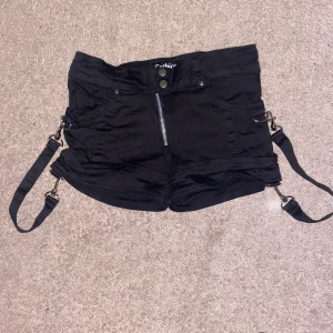 Svarta Gothicana shorts - Svarta Gothicana shorts med små hängslen längs höfterna.